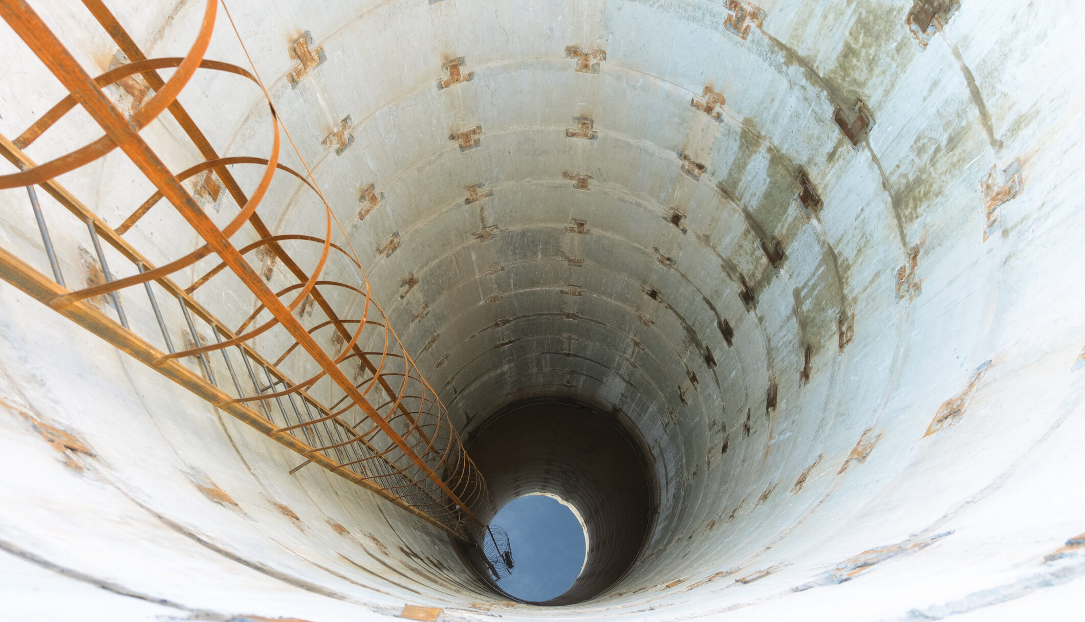 Deep reinforced concrete drainage well with metal stairs.